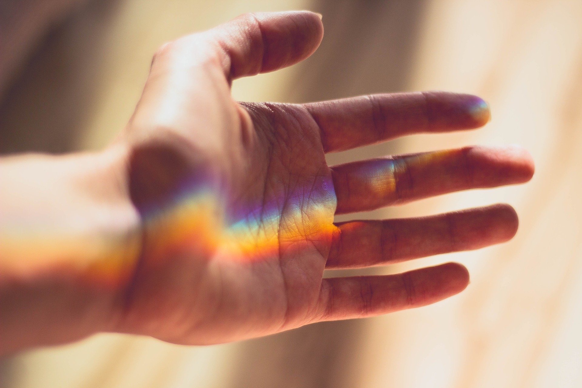 Eine Hand liegt offen im Licht, ein Regenbogenschimmer gleitet über die Haut. Die Geste wirkt einladend, fragil und voller stiller Bedeutung – wie ein Ja zum Berührtwerden.