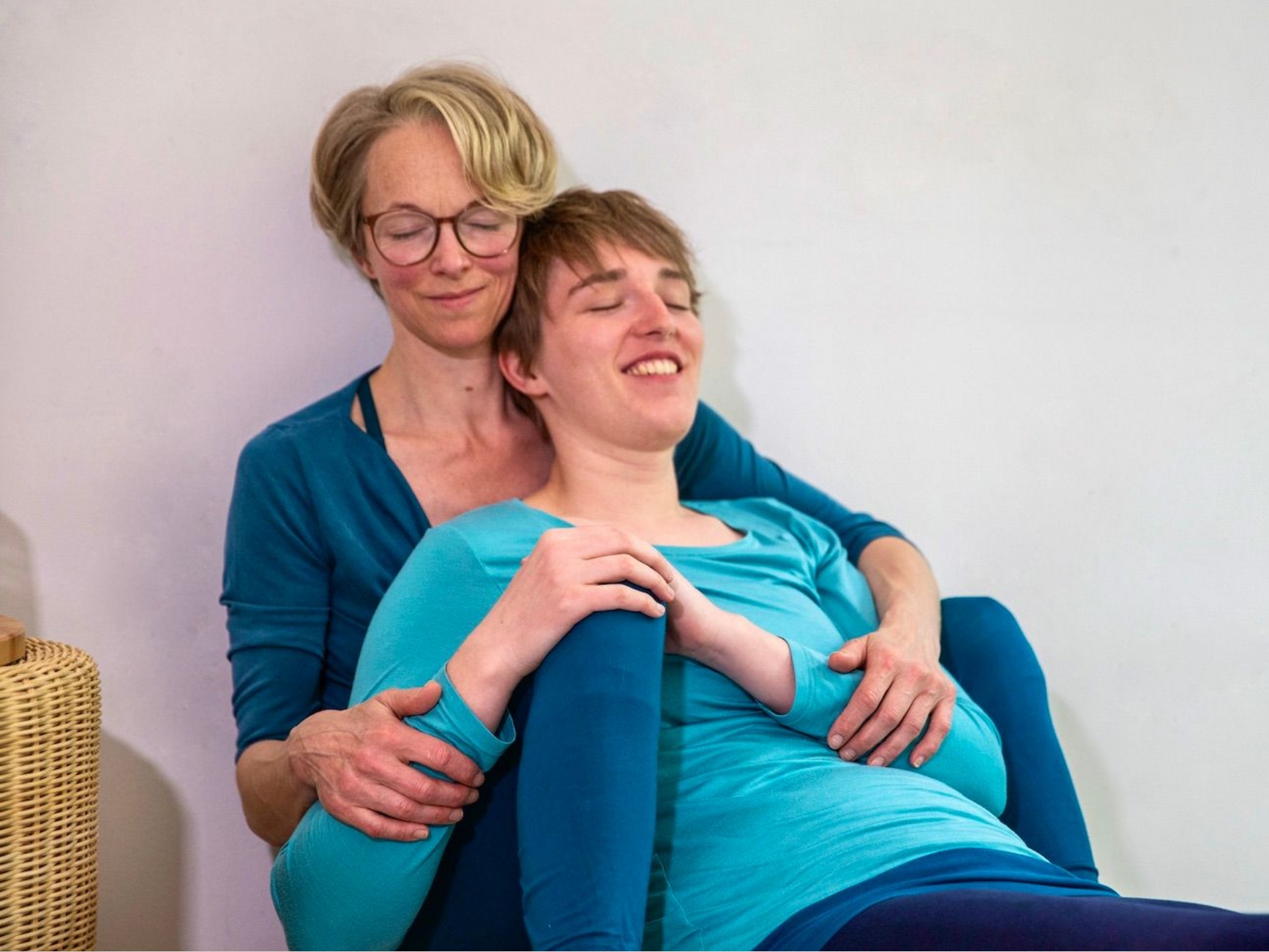 Zwei Frauen sitzen eng beieinander, eine lehnt sich ruhig an die andere, beide wirken entspannt und verbunden.