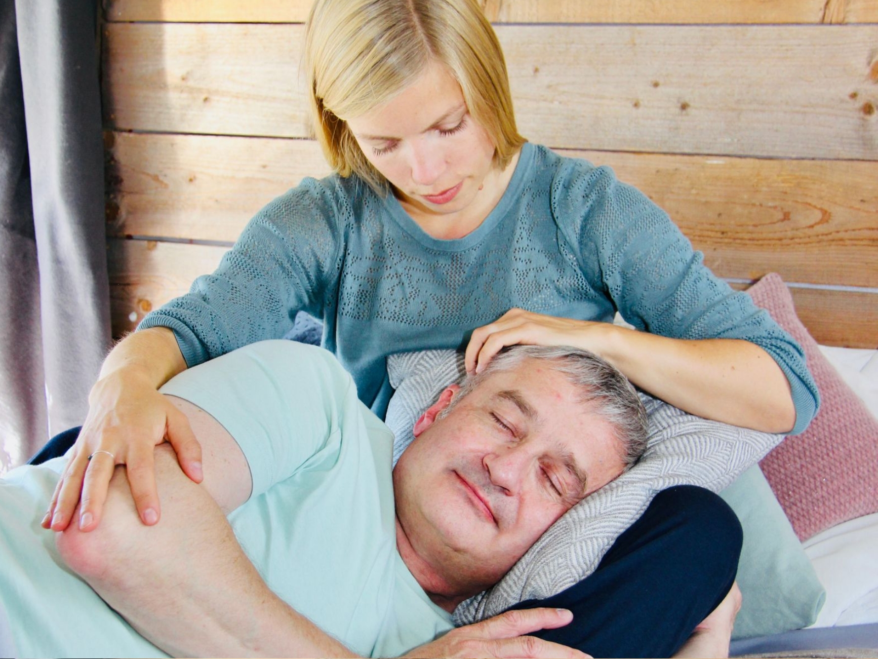 Kuscheltherapie mit älterem Klienten: Eine Kuscheltherapeutin hält einen älteren Mann auf ihrem Schoß und streichelt ihn achtsam.