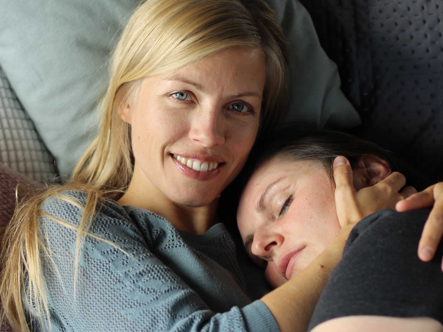 Kuscheltherapeutin strahlt in die Kamera, während sie eine Klientin sanft hält – ein Moment von Nähe, Sicherheit und professioneller Wärme.