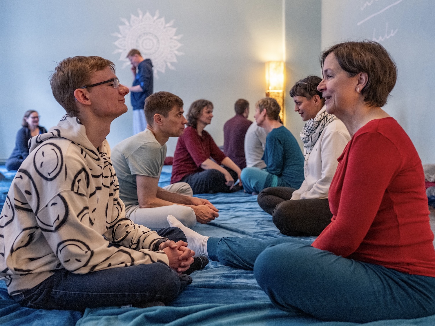 Menschen sitzen sich gegenüber und teilen Blickkontakt – Übungsrunde einer Kuschelparty im KuschelRaum, Raum für Vertrauen und Präsenz.