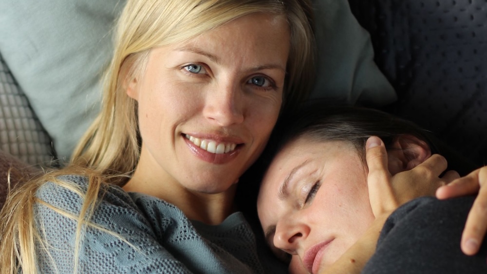 Kuscheltherapeutin strahlt in die Kamera, während sie eine Klientin sanft hält – ein Moment von Nähe, Sicherheit und Wärme.