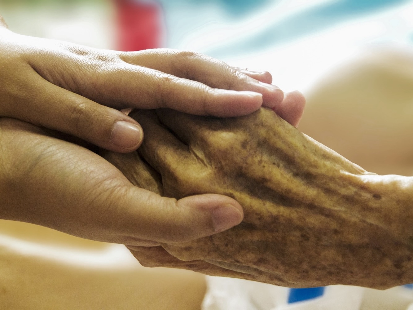 Eine jüngere Hand hält die Hand eines hochbetagten Menschen – Berührung im hohen Alter